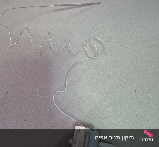 חוט מתכת מחובר לרכיב חשמלי על משטח אפור